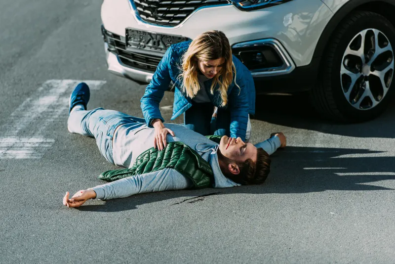 Femme bouleversée portant secours à un homme blessé allongé sur la chaussée après un accident de voiture